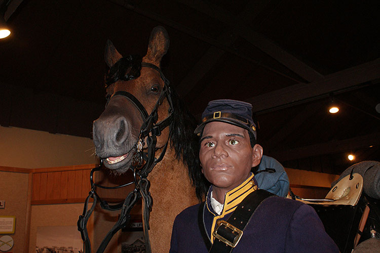 A mannequin standing with brown horse inside of Fort Sill National Historic Landmark & Museum.